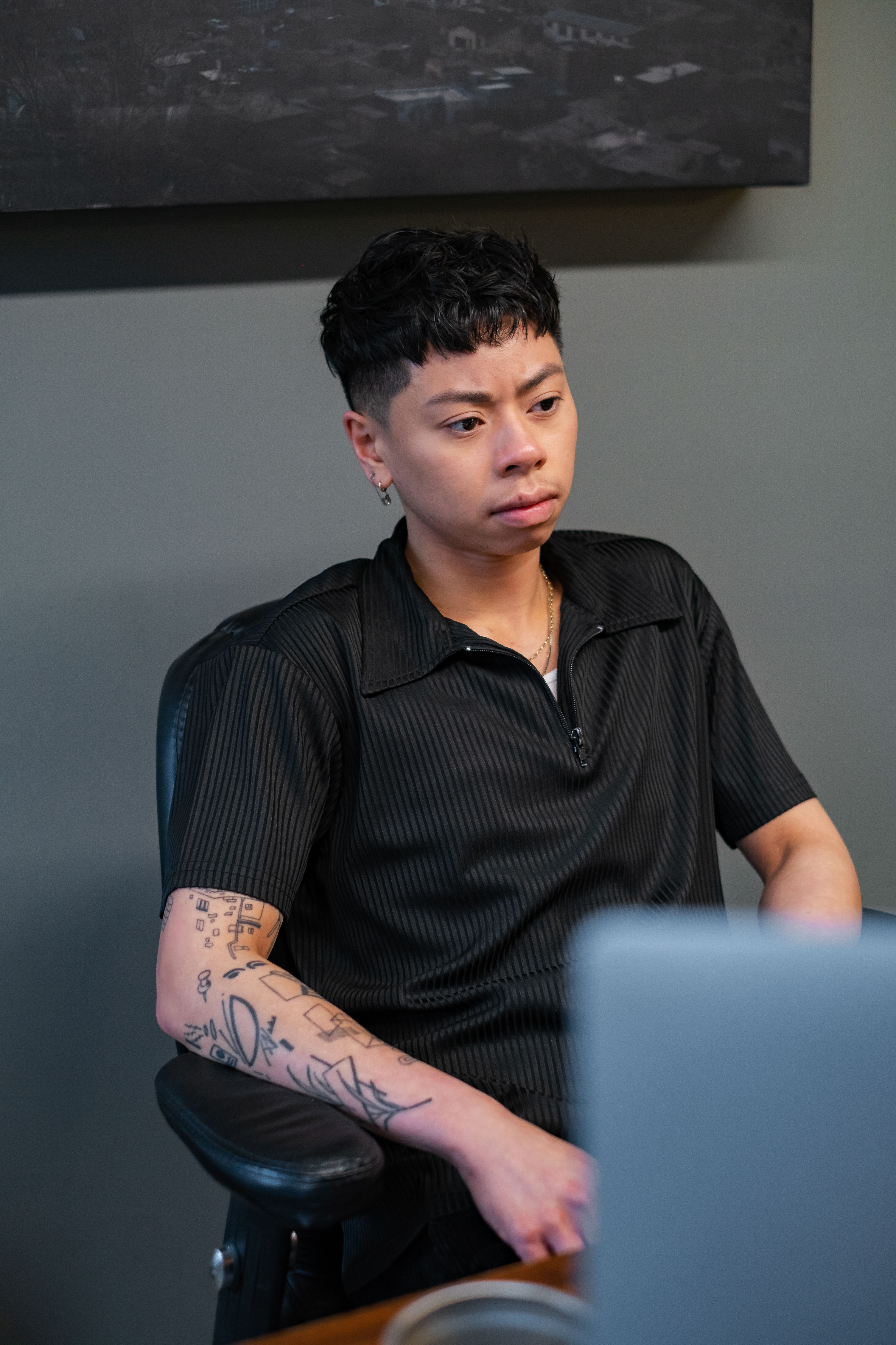 A non-binary person sitting behind a desk